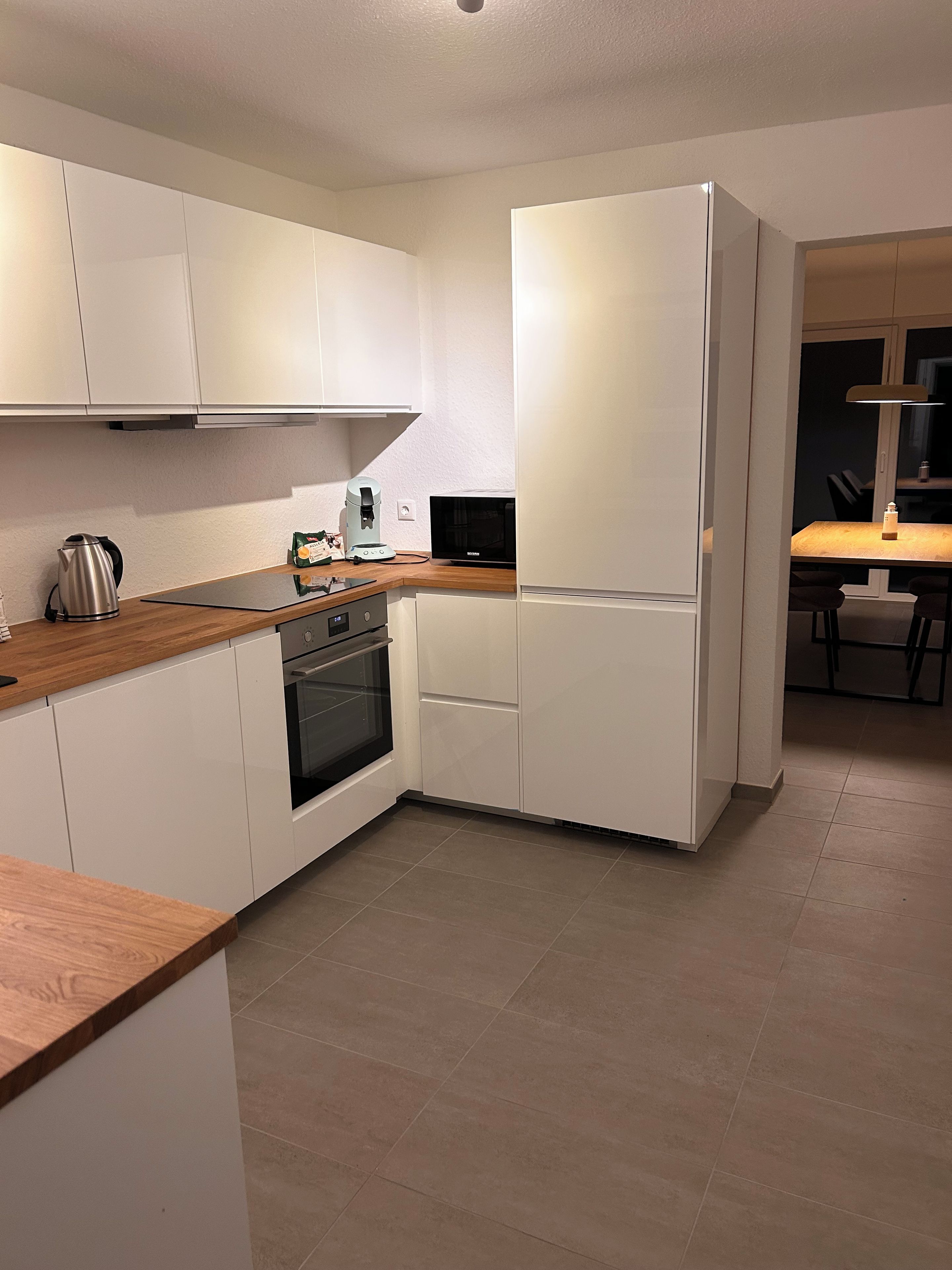 Een moderne keuken met witte kasten, een houten aanrecht, een inbouwoven en een koelkast.