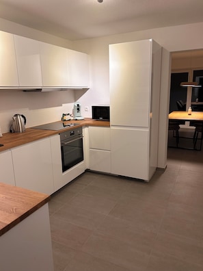 Una cocina moderna con armarios blancos, encimera de madera, horno empotrado y refrigerador.