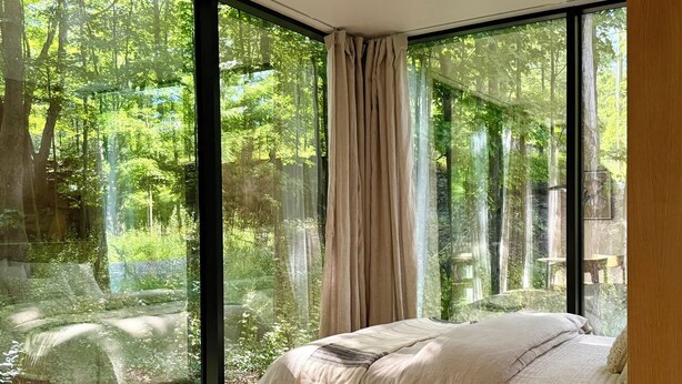 Een slaapkamer met een groot raam, een bed en uitzicht op een bos.
