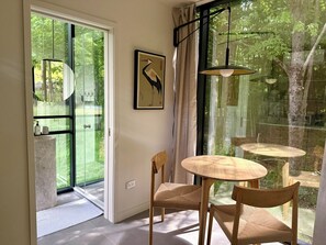 Ein Zimmer mit einer Schiebeglastür, die auf einen Balkon führt, einem runden Holztisch mit Stühlen, einem gerahmten Kunstwerk an der Wand und einer Pendelleuchte.