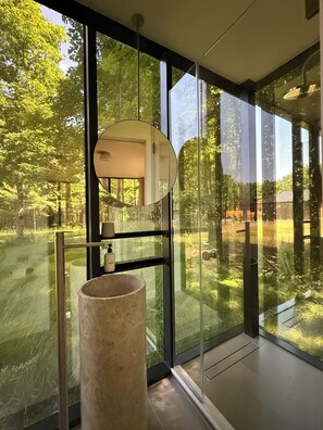 Ein modernes Badezimmer mit großem Fenster, rundem Spiegel und einem beigefarbenen Waschbecken.