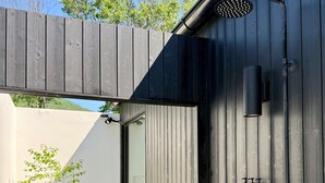Un'area doccia esterna moderna con un recinto in legno, un soffione metallico e un erogatore di sapone a parete.