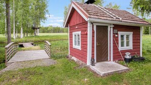 Una pequeña cabaña de madera roja con puerta, ventanas y chimenea.