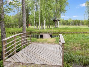 Un ponte di legno che attraversa un'acqua calma, circondato da una vegetazione rigogliosa e alberi.