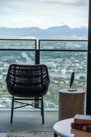 Ein Zimmer mit Blick auf Stadt und Berge. Ein schwarzer gewebter Sessel und ein kleiner runder Tisch mit einem Buch darauf.