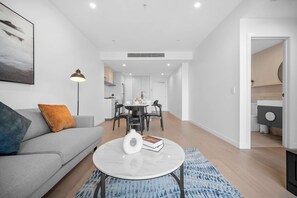 Un salon moderne avec un canapé gris, une table basse et un coin repas comprenant une table et des chaises.