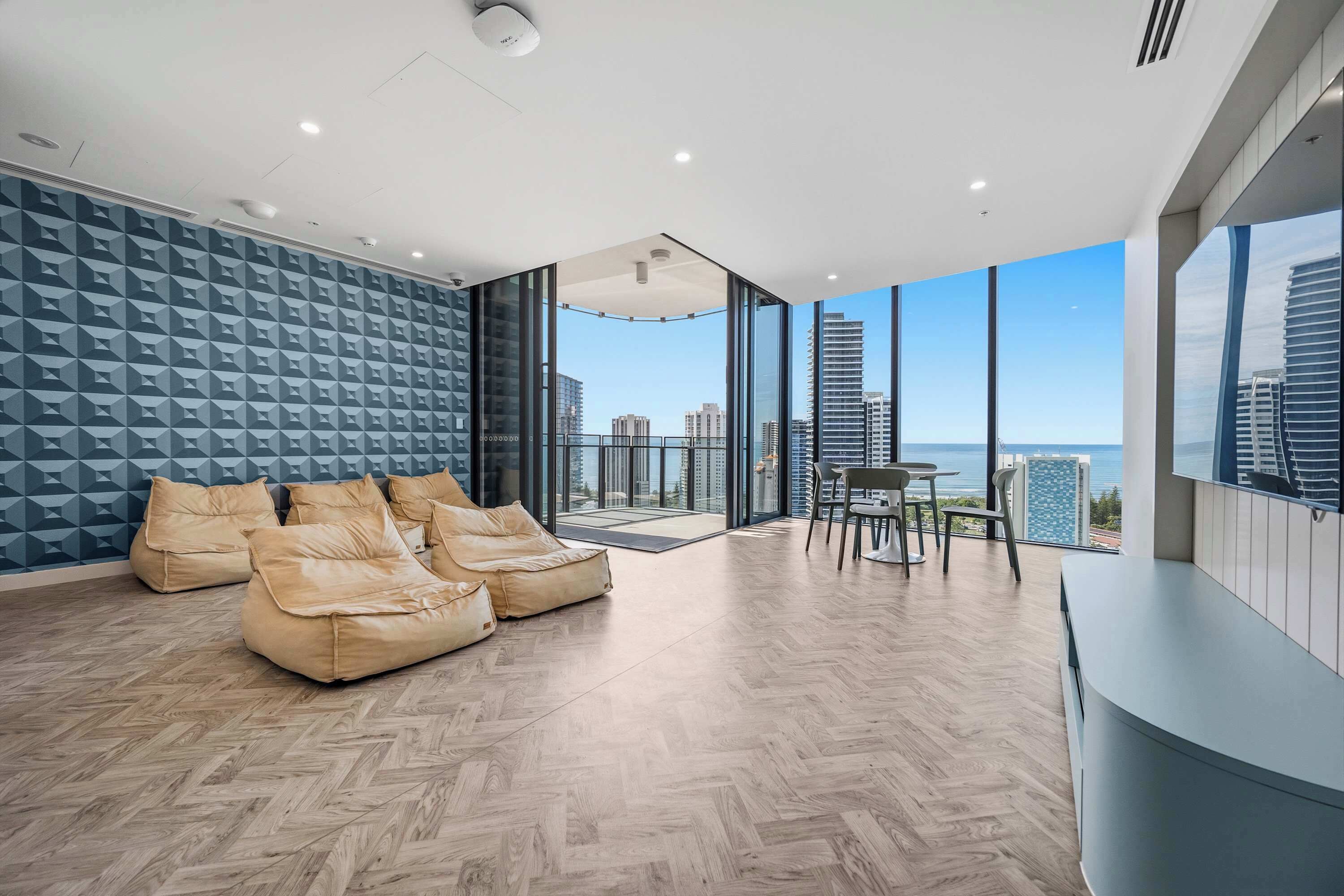 Una sala de estar moderna con piso de madera en espiga, un sofá modular y un comedor con vista al horizonte de la ciudad y al océano.