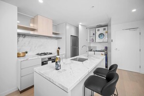 Une cuisine moderne dotée d’un plan de travail en marbre, d’une cuisinière à gaz, d’un four encastré, d’un réfrigérateur en acier inoxydable et d’un évier.