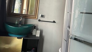A bathroom with a green sink, a mirror with a gold frame, a towel rack, and a trash bin. - Blossom Rue De Nava B&B (Reggio Calabria)