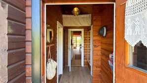 Un pasillo de madera con una lámpara colgante, una puerta que da a otra habitación y un ventanal con cortina de encaje.