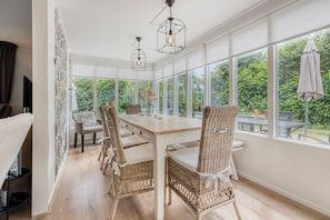 Een eethoek met een lange tafel, rieten stoelen en hanglampen.