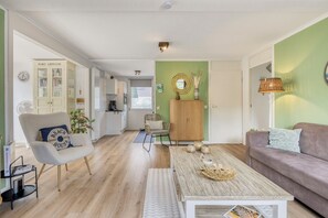 Ein modernes Wohnzimmer mit Sofa, Sessel, Couchtisch und einer Küche im Hintergrund.