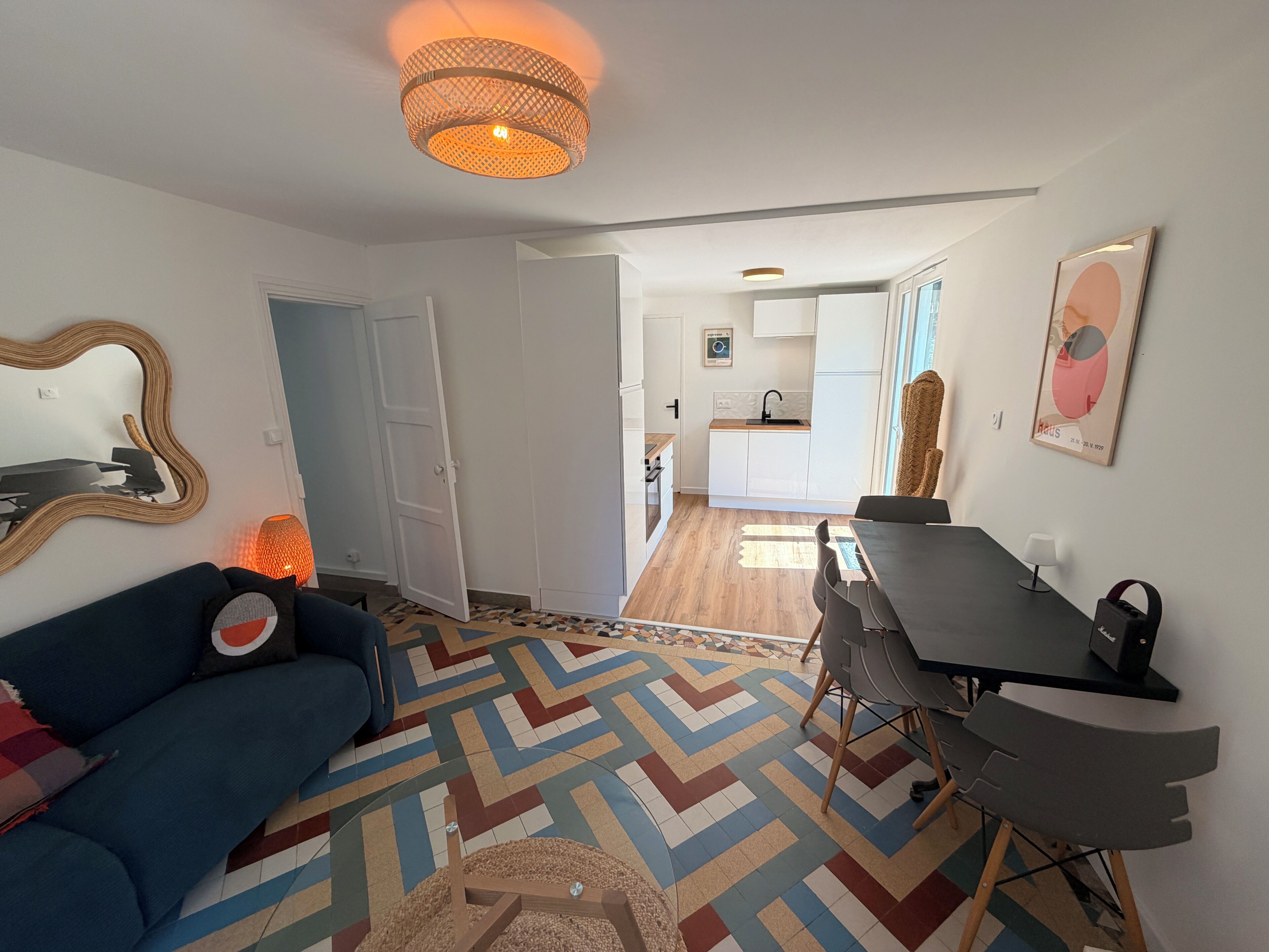 Una sala de estar con un sofá, una mesa de comedor con sillas, una cocina al fondo y un piso estampado.