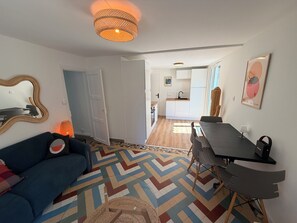 A living room with a sofa, a dining table with chairs, a kitchen in the background, and a patterned floor. - MAISON HORTENSE: Sleeps 8, 3 minutes from the beach and downtown (Saint-Brevin-les-Pins)