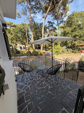 A patio with a table and chairs, a white umbrella, and a view of trees and a building. - MAISON HORTENSE: Sleeps 8, 3 minutes from the beach and downtown (Saint-Brevin-les-Pins)