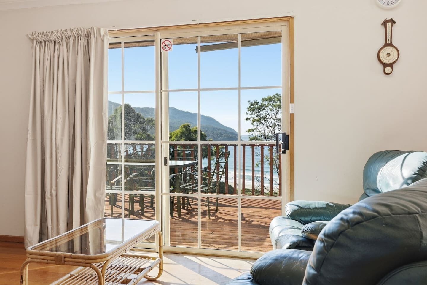 A room with a sliding glass door leading to an outdoor deck, a wicker chair, a sofa, and a wall clock.