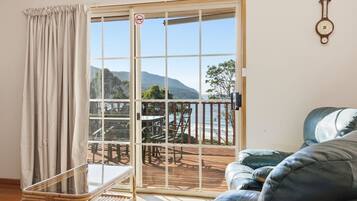 A room with a sliding glass door leading to an outdoor deck, a wicker chair, a sofa, and a wall clock.