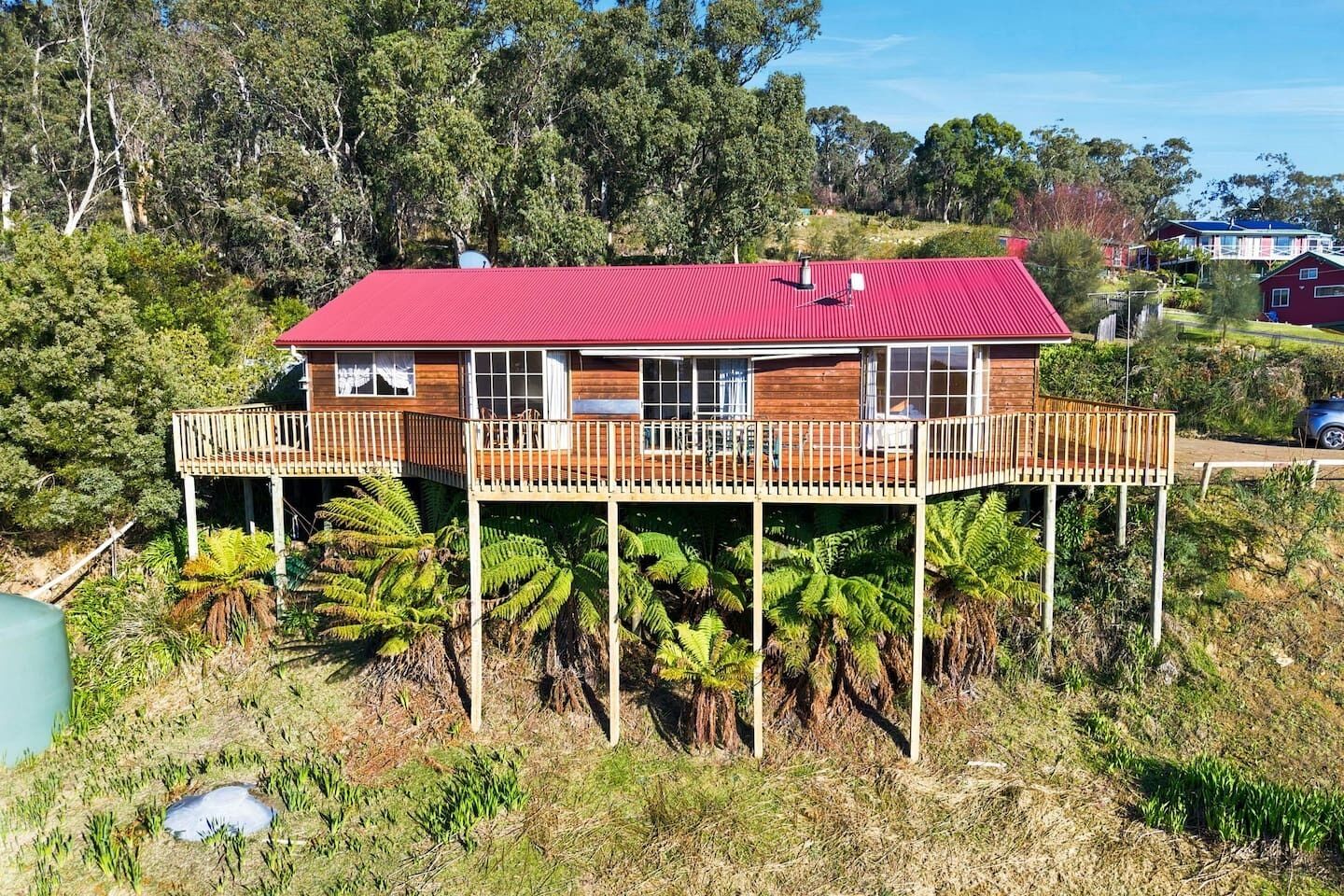 A two-story wooden house with a red roof, a deck, and a pool.