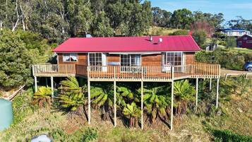 A two-story wooden house with a red roof, a deck, and a pool.