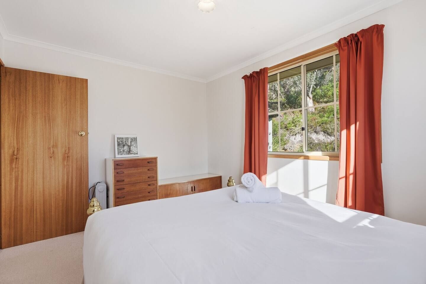 Une chambre à coucher avec un grand lit, une armoire en bois, une petite commode et une fenêtre avec des rideaux.