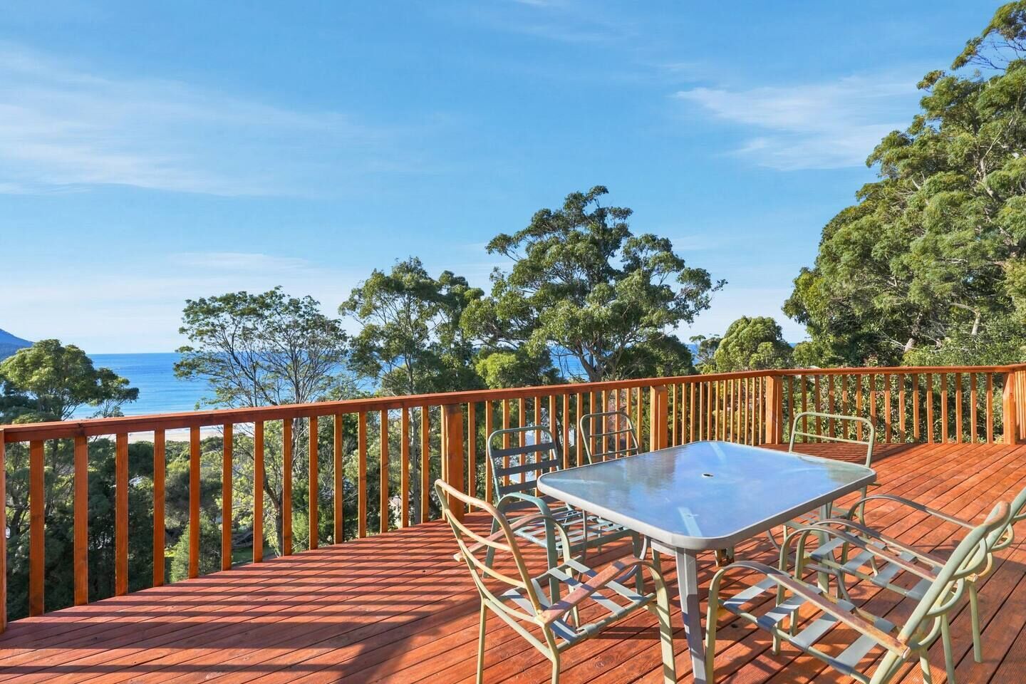 A wooden deck with a table and chairs, overlooking a body of water and trees.