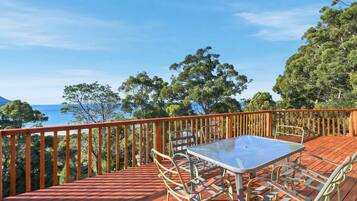 A wooden deck with a table and chairs, overlooking a body of water and trees.
