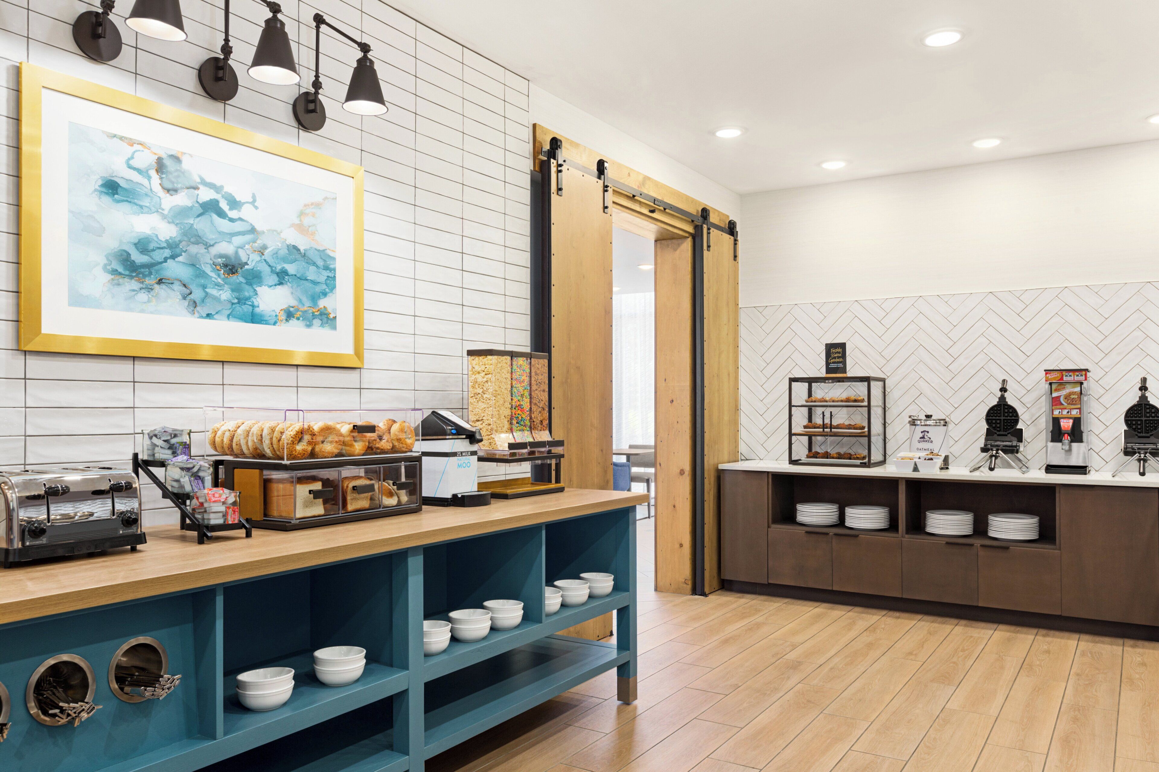 Un comptoir pour le petit-déjeuner équipé d’une machine à café, de bagels et d’un appareil à gaufres.
