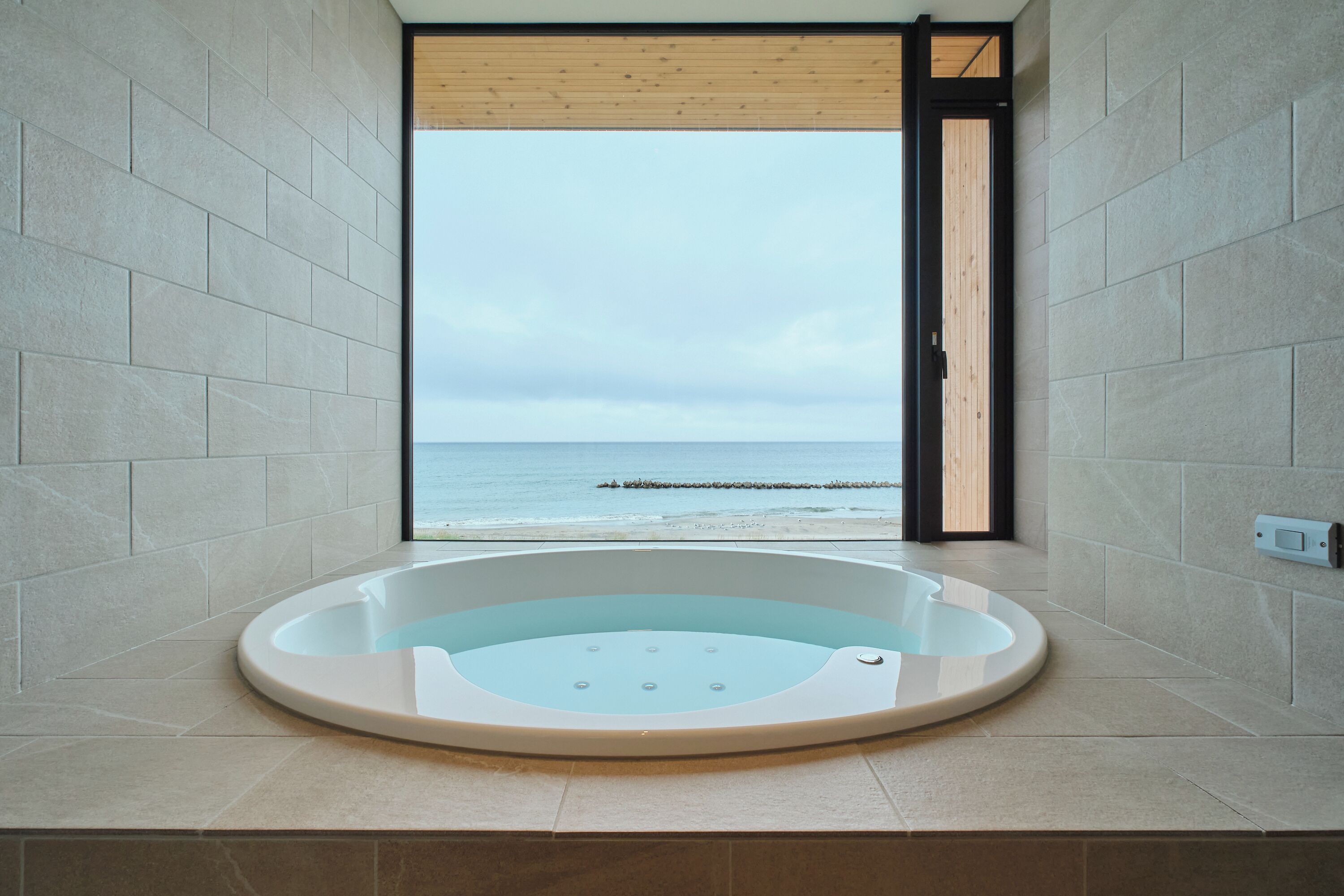 Un baño moderno con una bañera grande, vistas al mar y una puerta de madera.