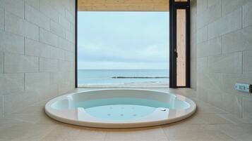 Un baño moderno con una bañera grande, vistas al mar y una puerta de madera.