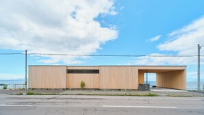 A modern building with a wooden facade, a covered entrance, and a view of the sea. - ATUY ISHIZAKI (Hakodate City)
