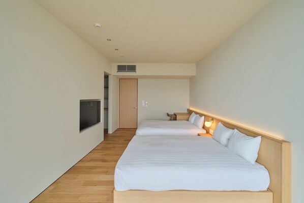 A hotel room with two beds, a TV mounted on the wall, and a wooden floor. - ATUY ISHIZAKI (Hakodate City)
