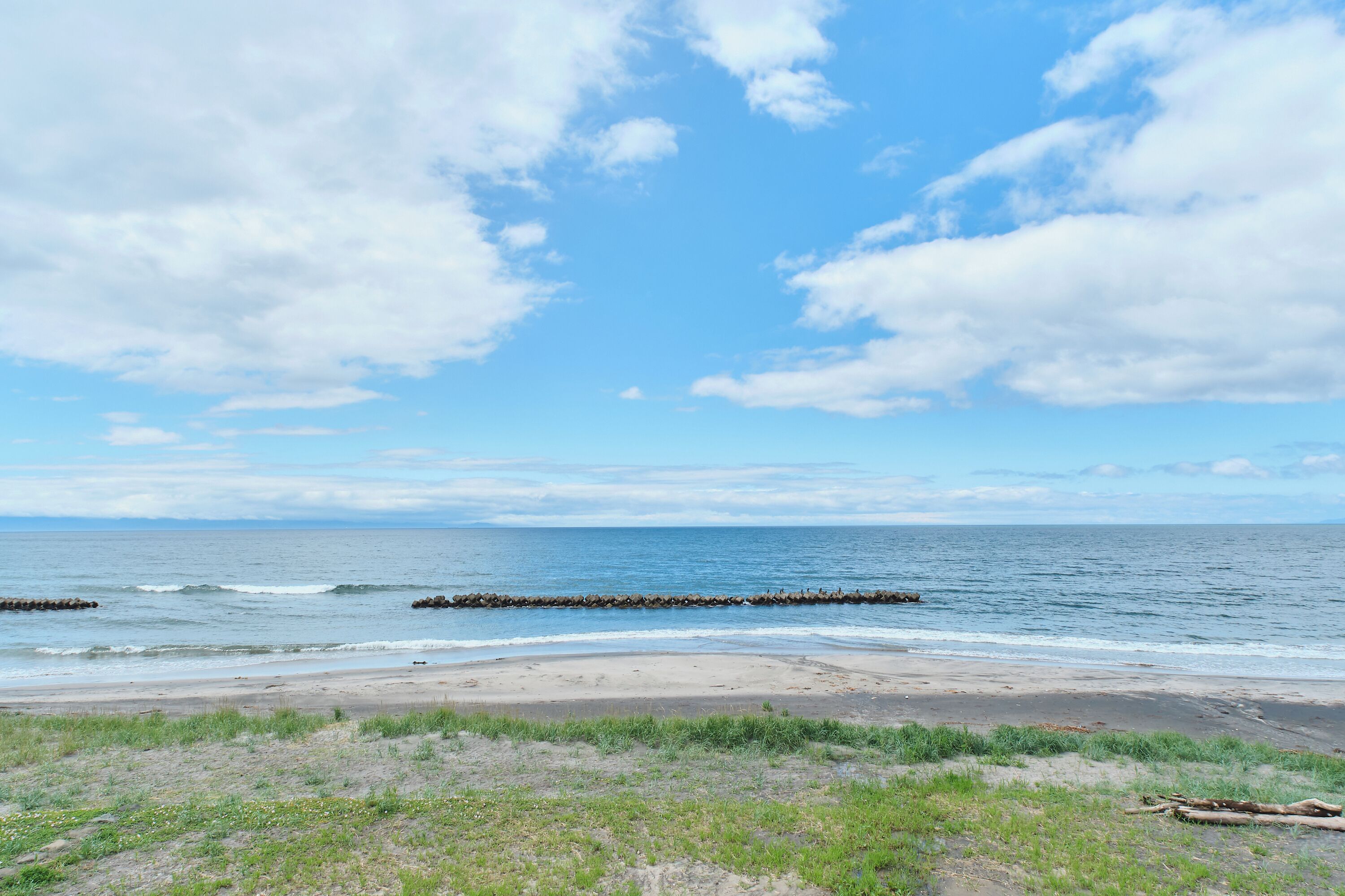A beach with a clear sky, calm sea, and a rocky breakwater.