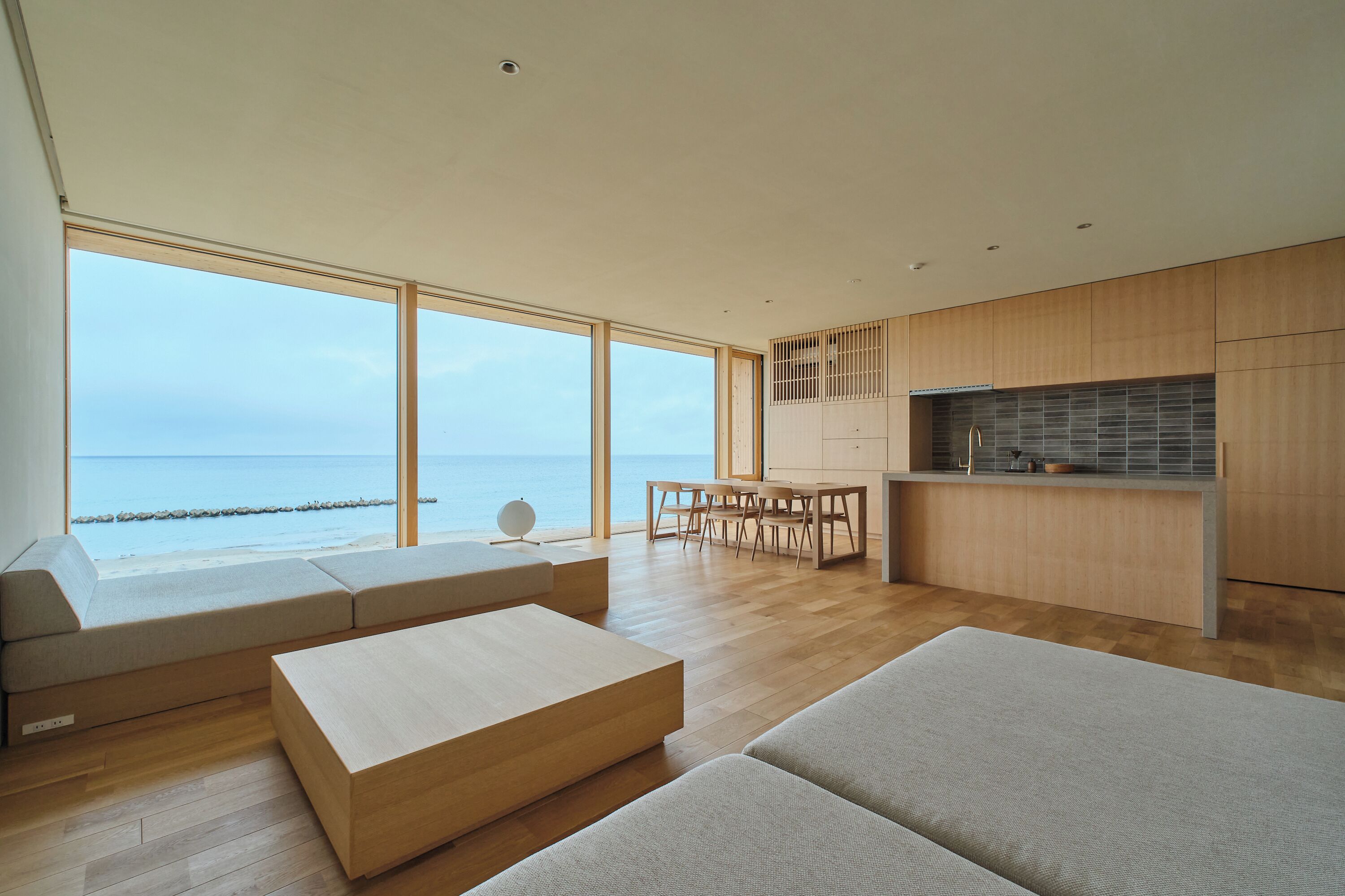 A modern living space with a large window overlooking the sea, a dining area, and a kitchen.