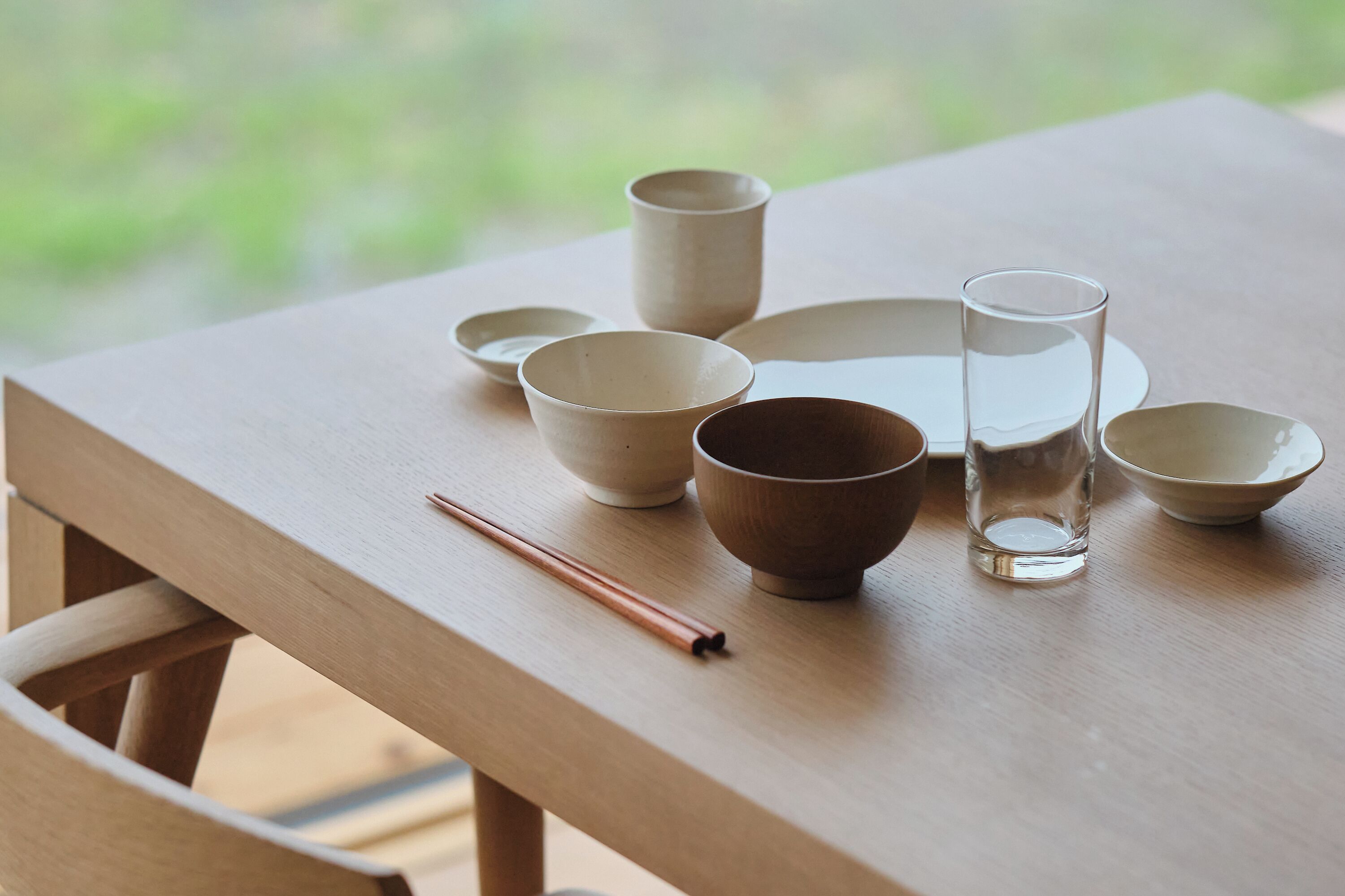 A wooden table with various ceramic bowls and a glass, arranged neatly.