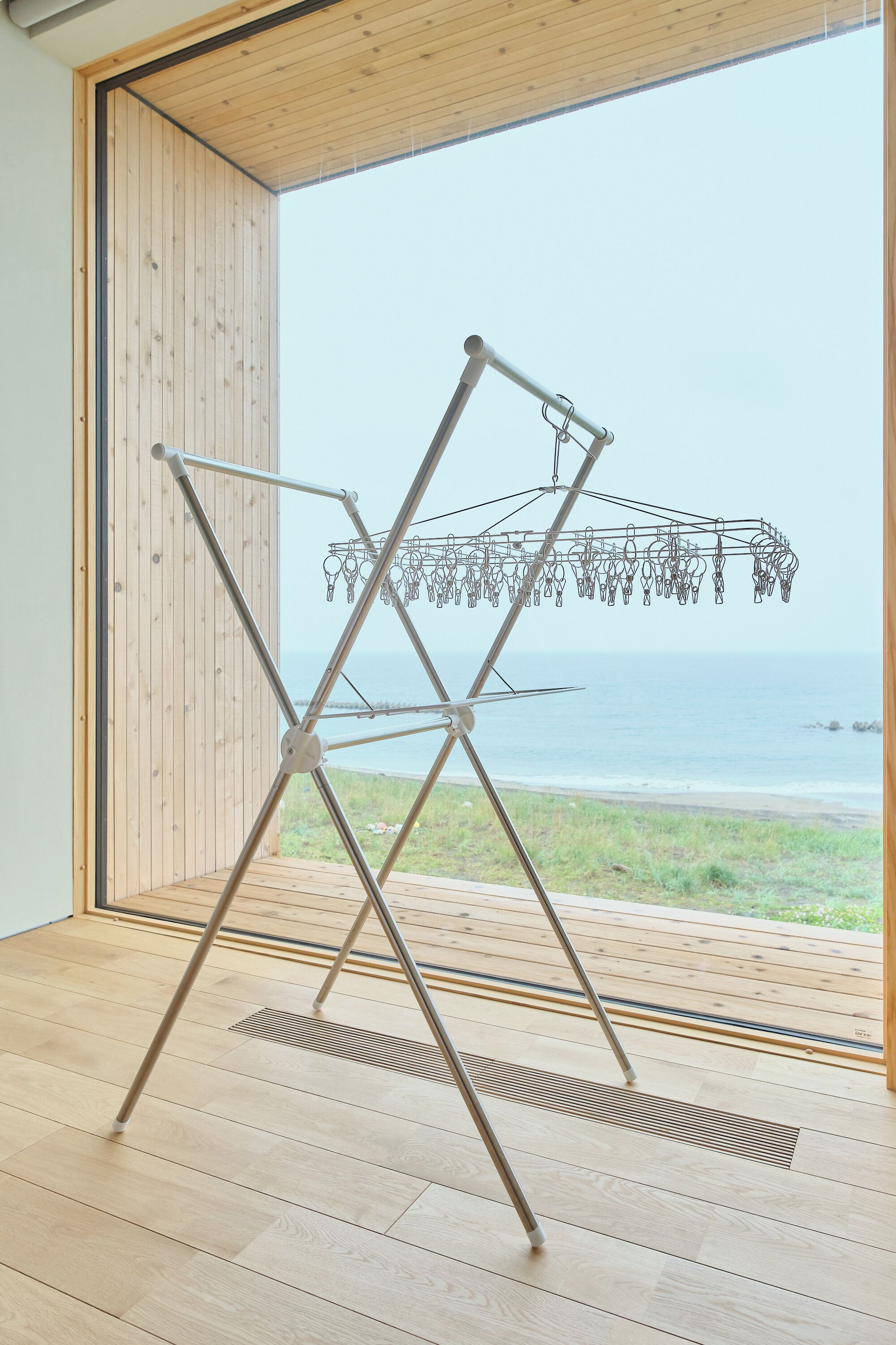 A room with a wooden floor, a metal drying rack, and a view of the ocean.