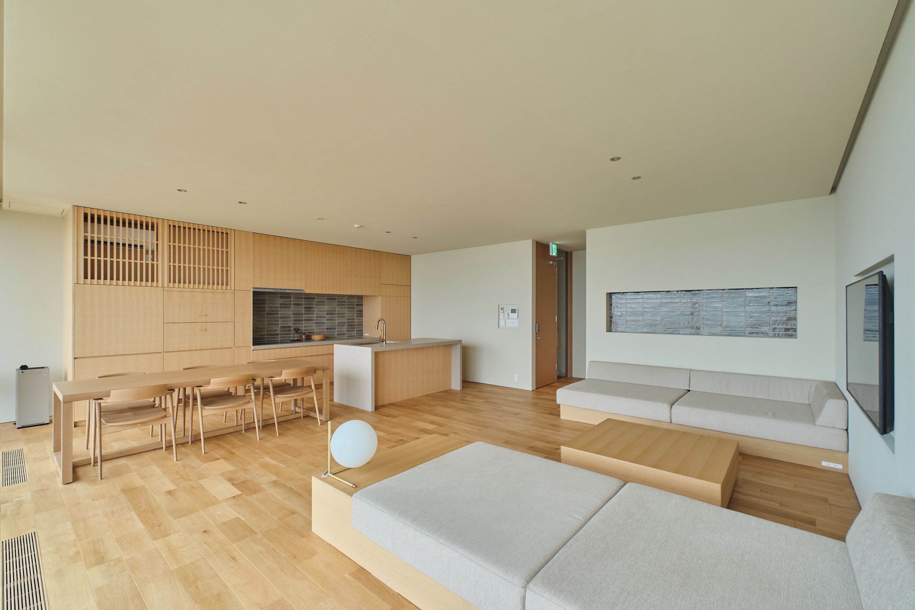 A modern living room with a sofa, a dining table, and a kitchen area with wooden cabinets and a built-in stove.
