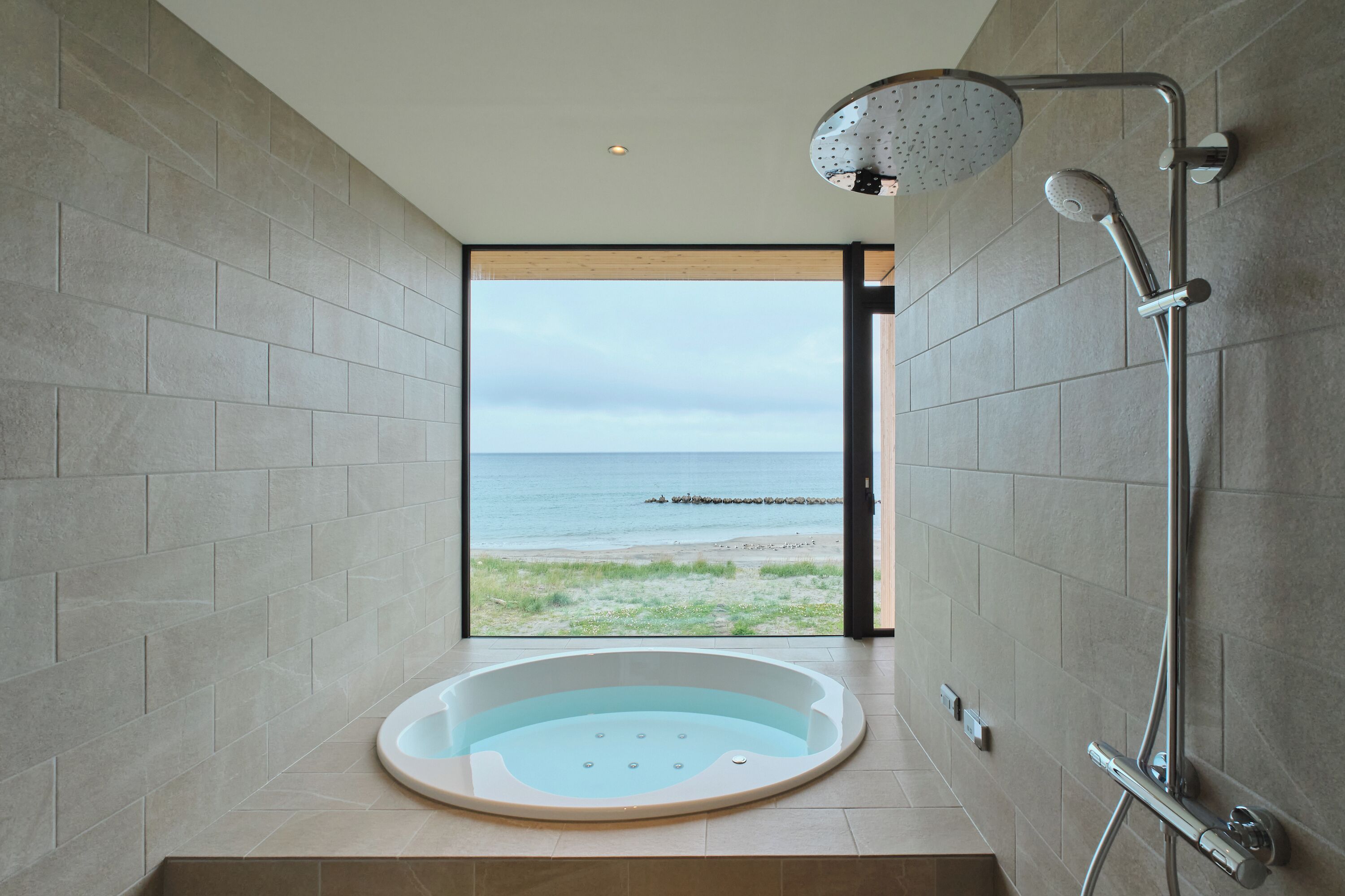 A modern bathroom with a large bathtub, a shower, and a view of the sea.
