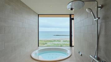 A modern bathroom with a large bathtub, a shower, and a view of the sea.