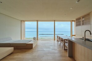 A modern interior with a kitchen, dining area, and a large window overlooking the sea. - ATUY ISHIZAKI (Hakodate City)