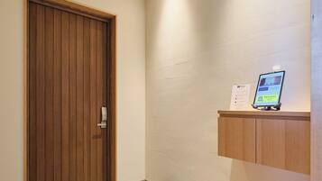 A hallway with a wooden door, a stone slab, a wooden floor, and a wall-mounted shelf with a tablet.