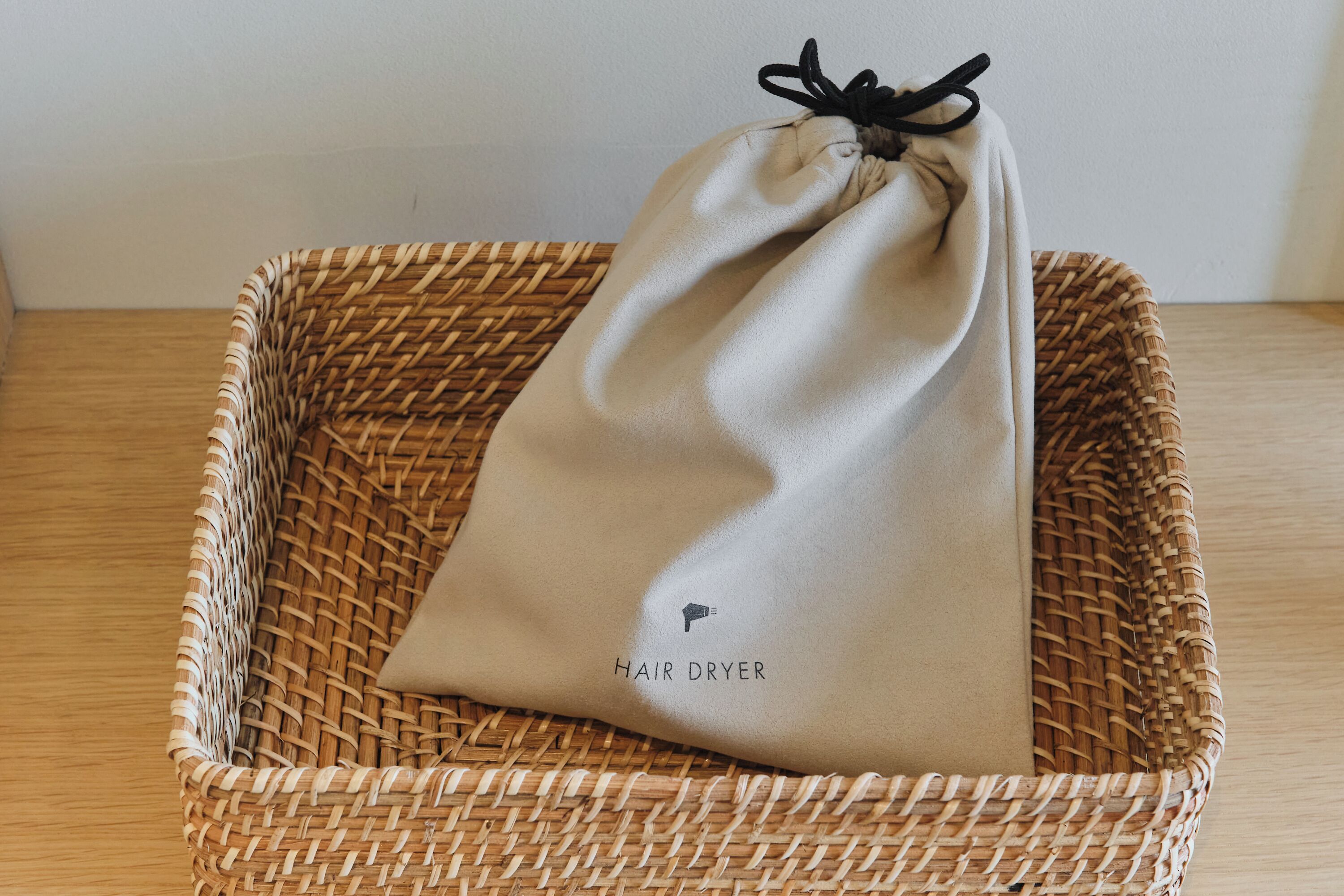 A woven basket containing a beige drawstring bag labeled 'HAIR DRYER.'