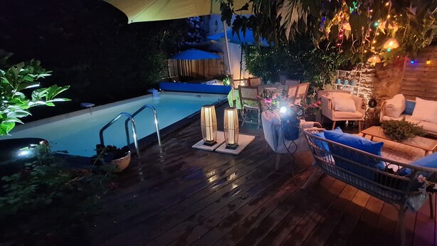 Un área de piscina con terraza de madera, sillas de descanso y luces colgantes.