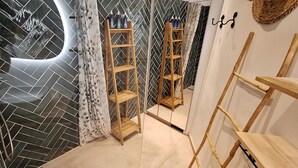 Un baño con patrón de mosaico de espiga, un estante escalonado de madera y un espejo que refleja el ambiente.