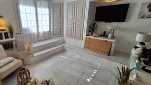 Una sala de estar con un sofá, un televisor, una ventana con cortinas, una mesita con velas y una planta.