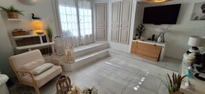 A living room with a sofa, a TV, a window with curtains, a small table with candles, and a plant. - 10 km from the beaches; Renovated village house, quiet location; Sleeps 6–8; Pool and Jacuzzi (Roquebrune-sur-Argens)