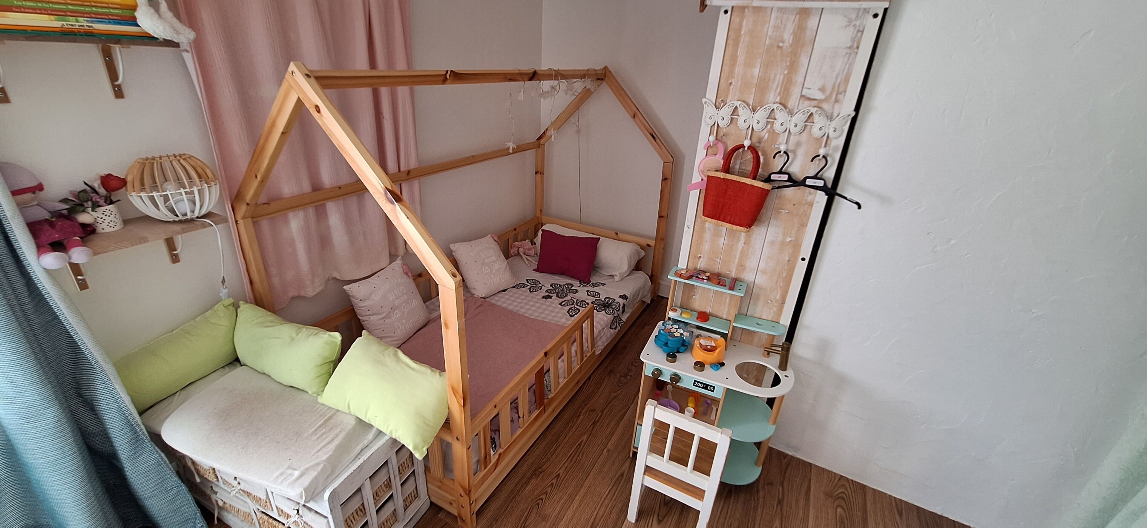 A child's bedroom with a wooden bunk bed, a small desk, and a hanging shelf with toys.