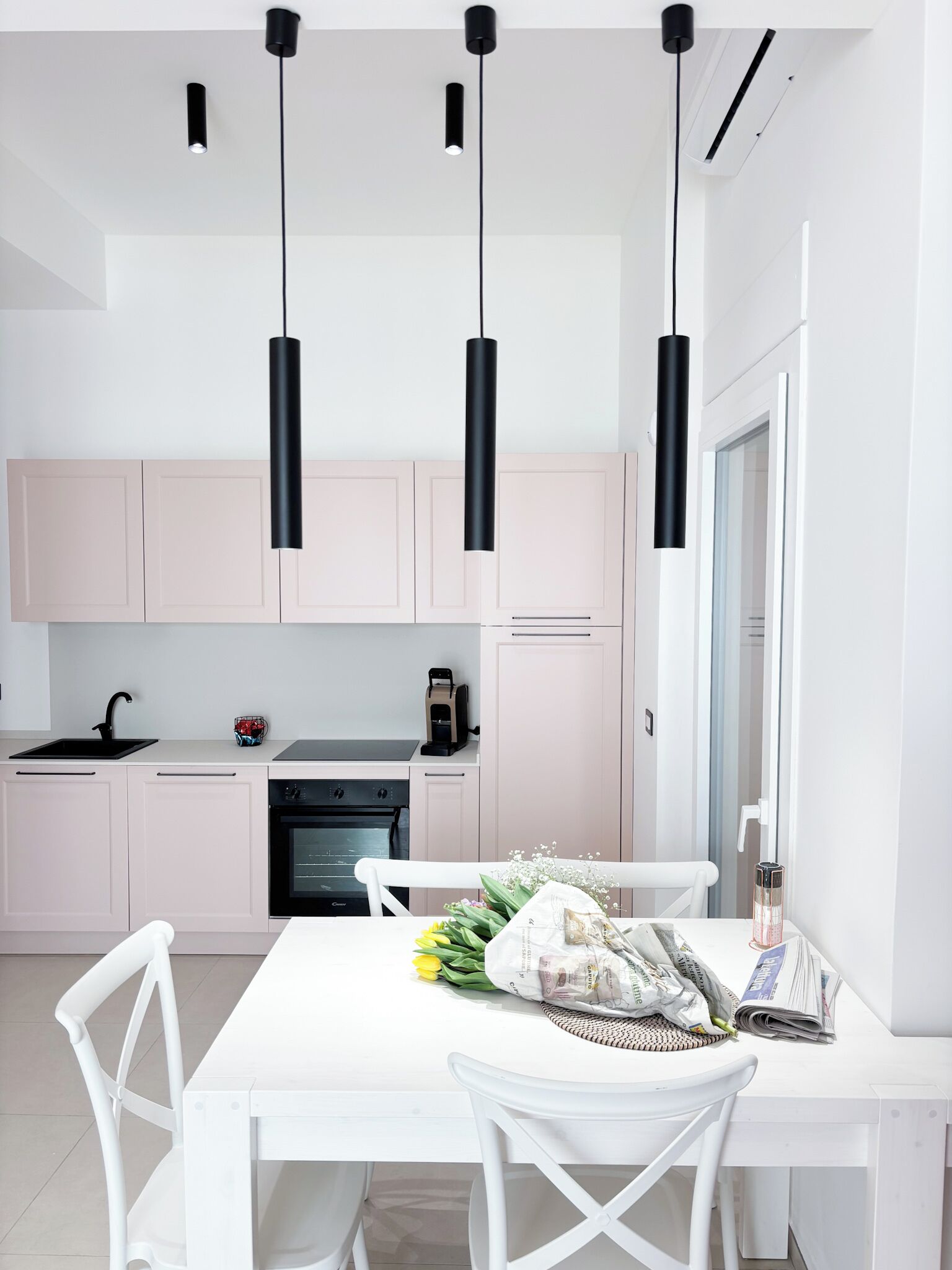A modern kitchen with white cabinets, a black oven, and pendant lights.