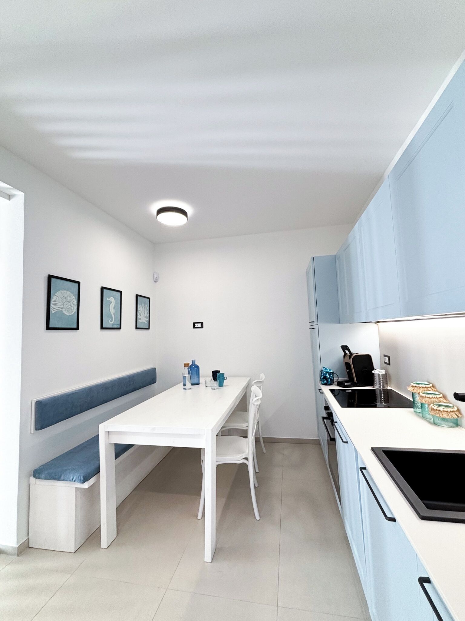Una cucina compatta con un tavolo bianco, mobili azzurri e una panca.