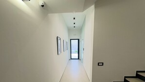 Un pasillo con cuadros en la pared, una puerta al final y una escalera a la derecha.
