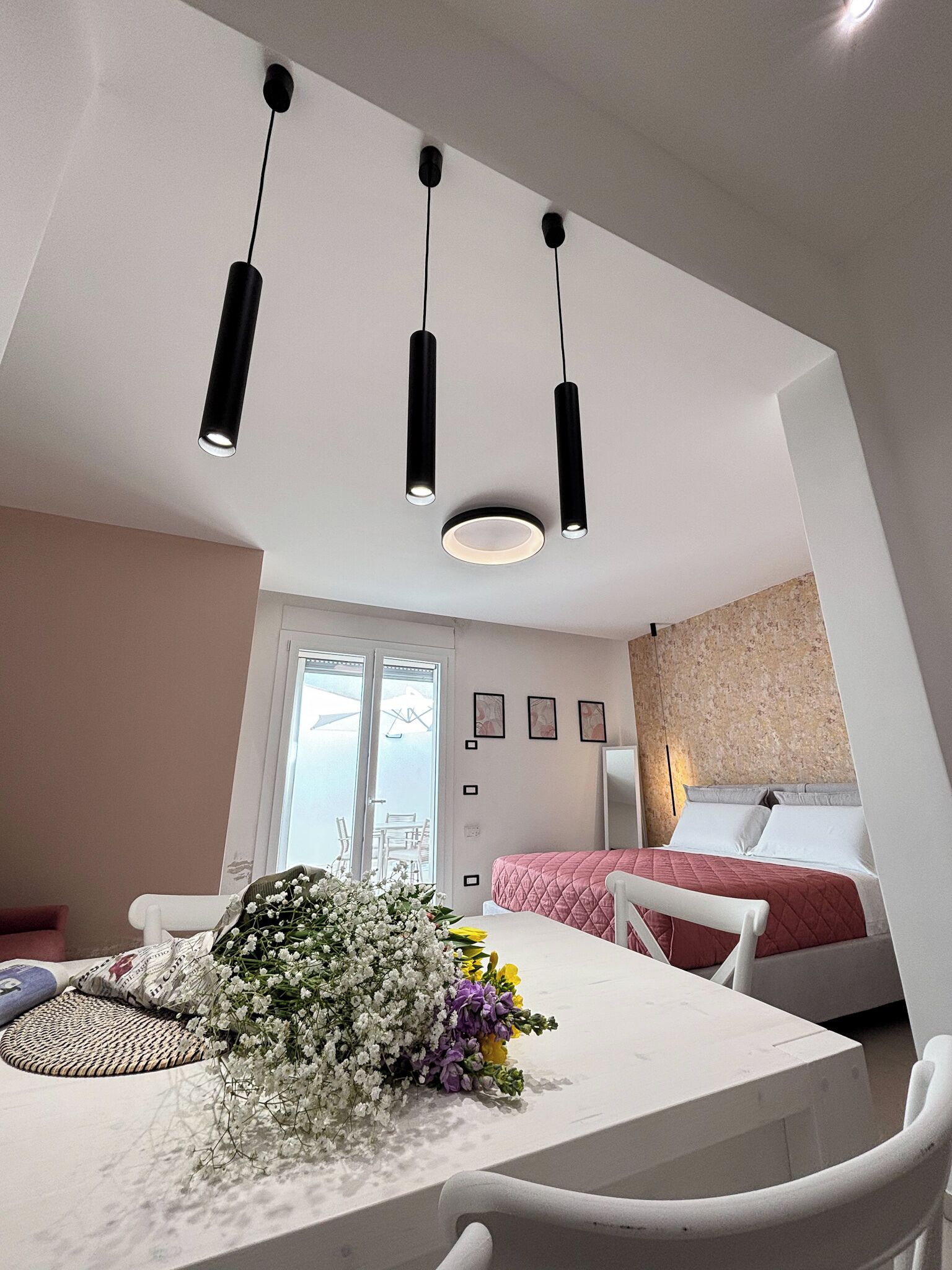 A modern bedroom with a bed, a white wall, and a window.